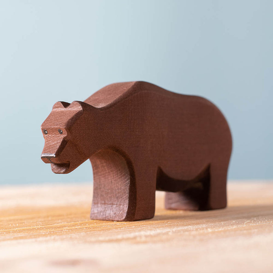 Close up of the Bumbu brown wooden bear toy on a wooden worktop in front of a blue background