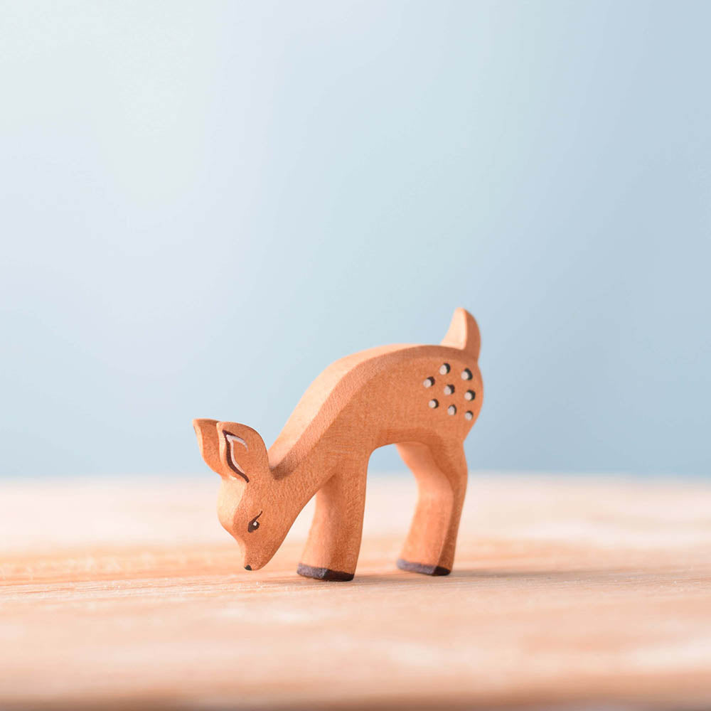 Bumbu childrens brown wooden eating fawn toy figure stood on a wooden worktop in front of a blue background