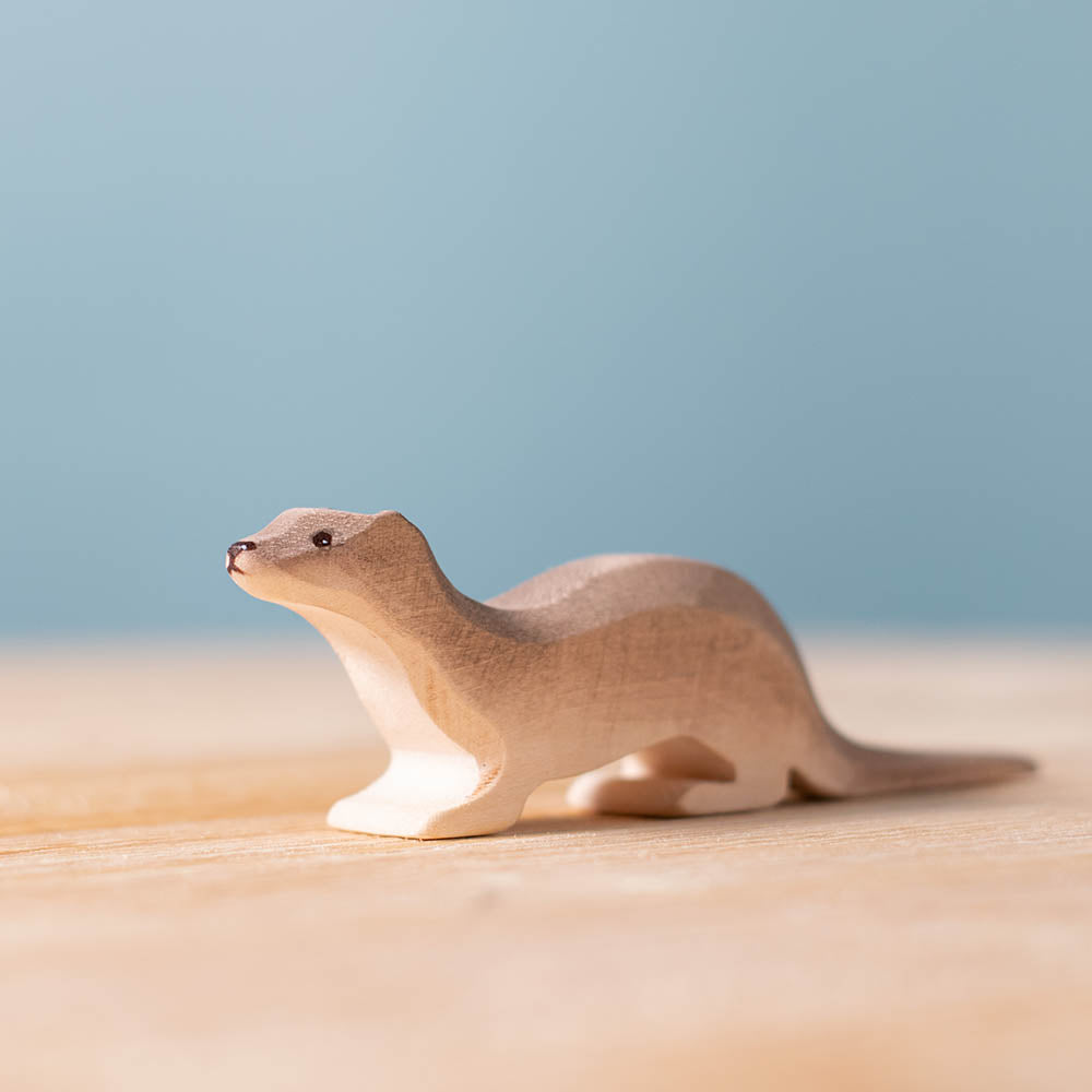 Close up of the Bumbu hand carved wooden otter toy on a wooden surface in front of a blue background