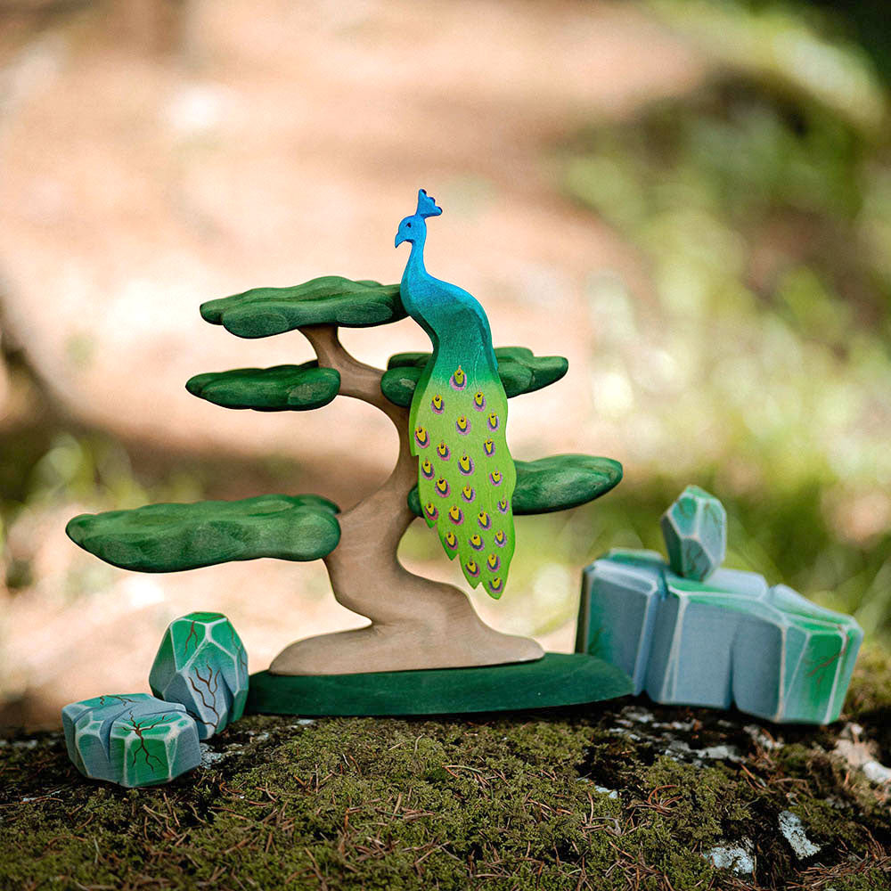 Close up of a Bumbu wooden Peacock and Bonsai tree figure on some moss in front of a blurred beige background