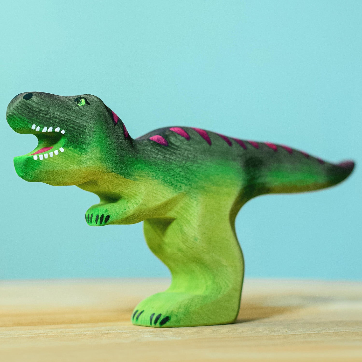 Wooden toy adult T-Rex in vibrant shades of green and purple. The T-Rex stands upright with its jaws open in a forward stance. The toy has painted teeth