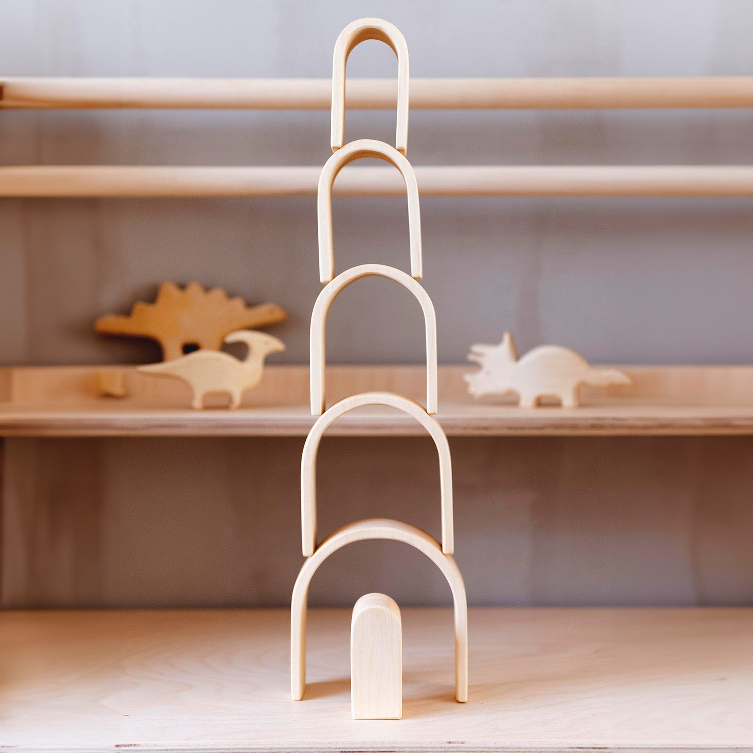 Bumbu Natural Wooden Stacking Arches. The toy sits on a white surface an adult hand is shown to denote scale.