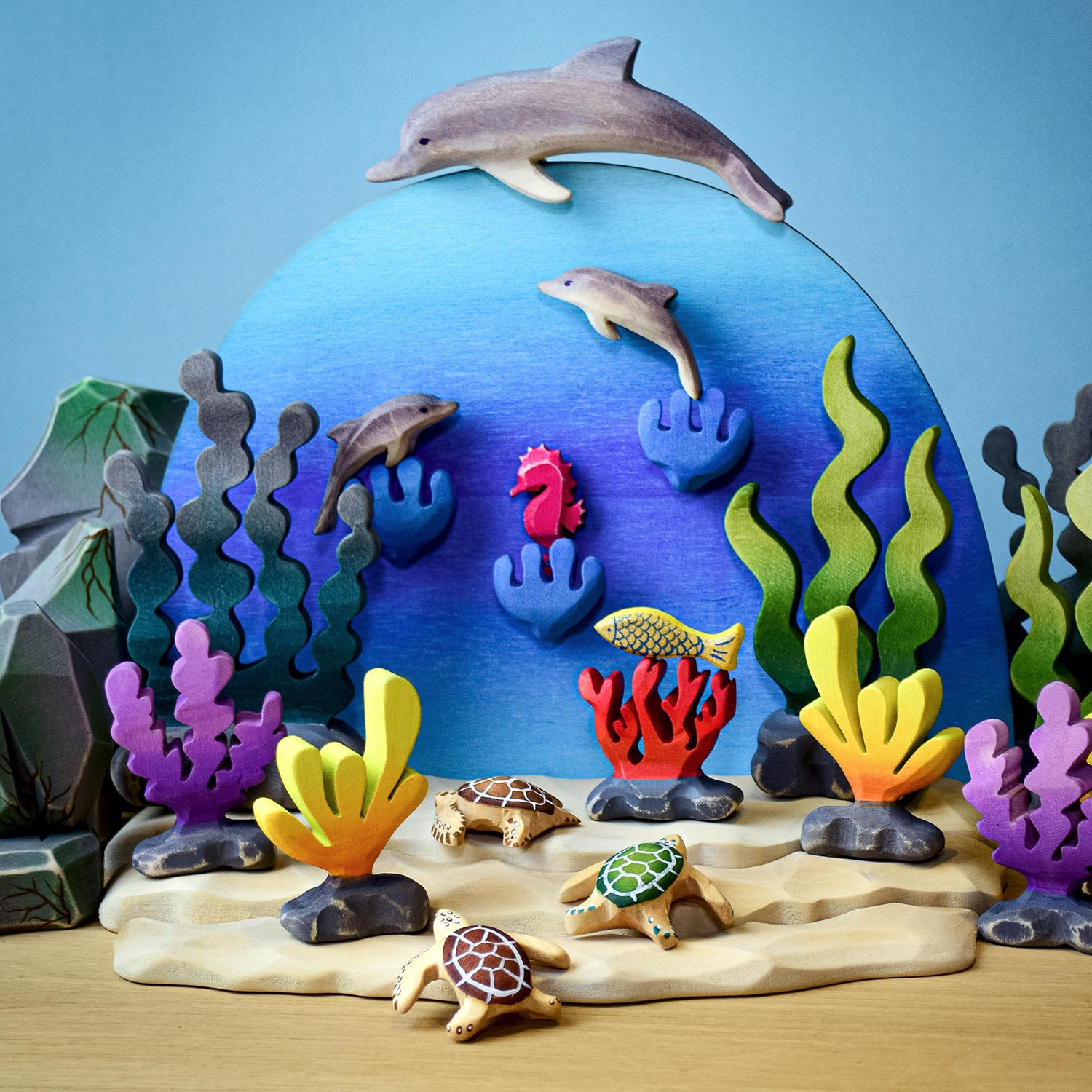 Bumbu Wooden Baby Dolphin. The toy is set amongst an underwater scene with other dolphins