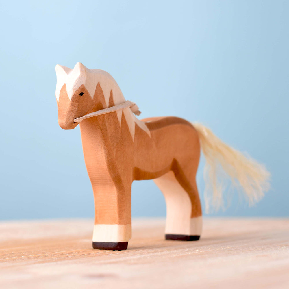 Bumbu eco-friendly golden brown wooden horse toy on a wooden worktop in front of a blue background