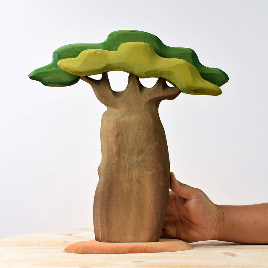 Hand reaching out to hold the Bumbu handmade wooden Baobab tree on a light wooden table