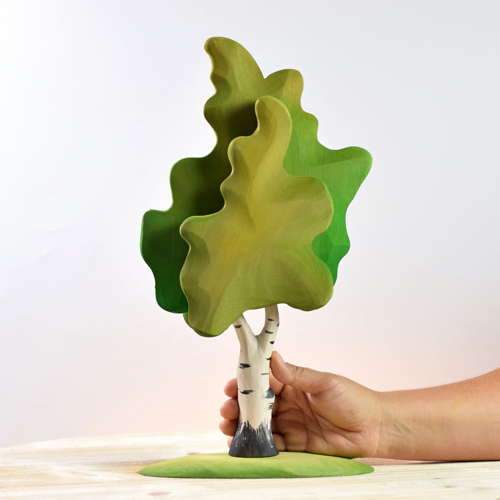 Hand holding the Bumbu eco-friendly handmade wooden birch tree on a white wooden background