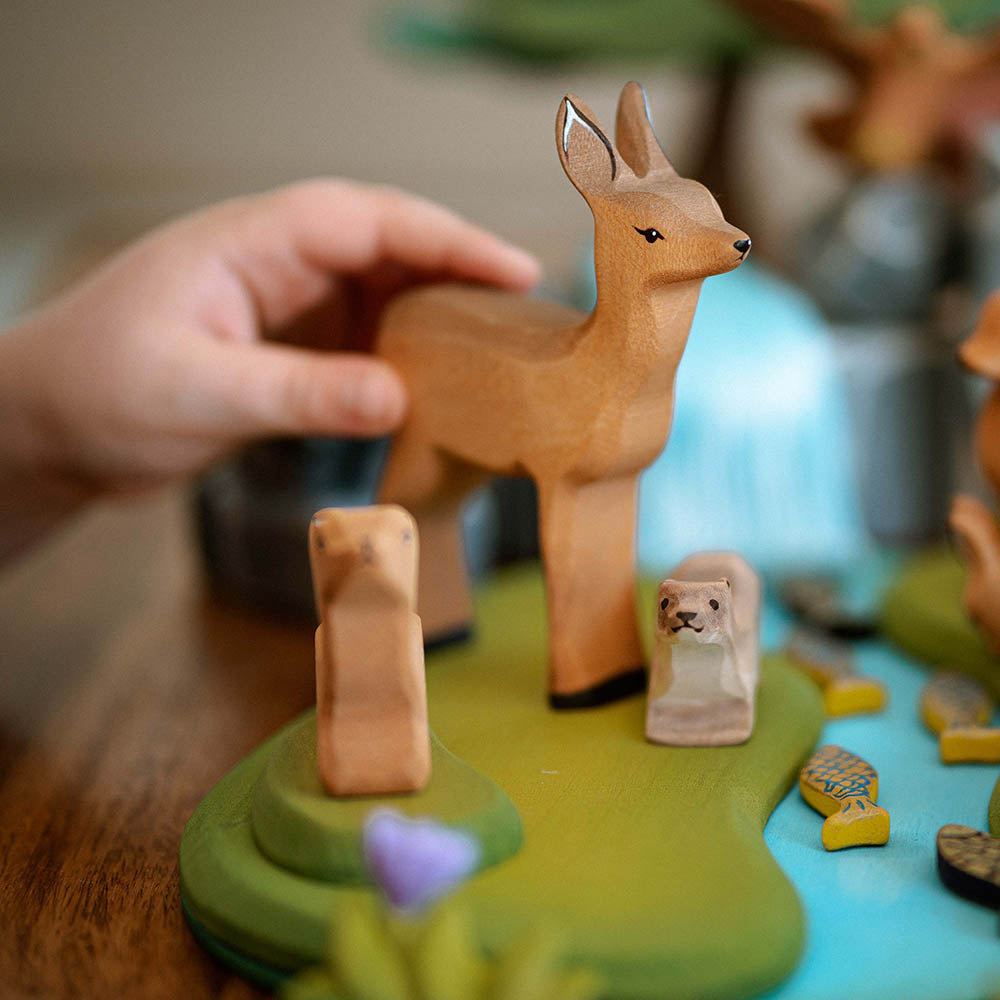 Bumbu wooden deer animal figures stood on a wooden waterfall scene in front of some large toy trees