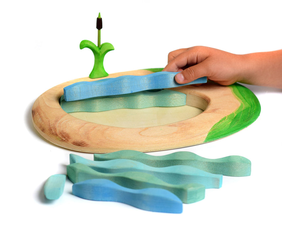 Hand moving the pieces of a Bumbu lake and cattail eco-friendly wooden puzzle on a white background