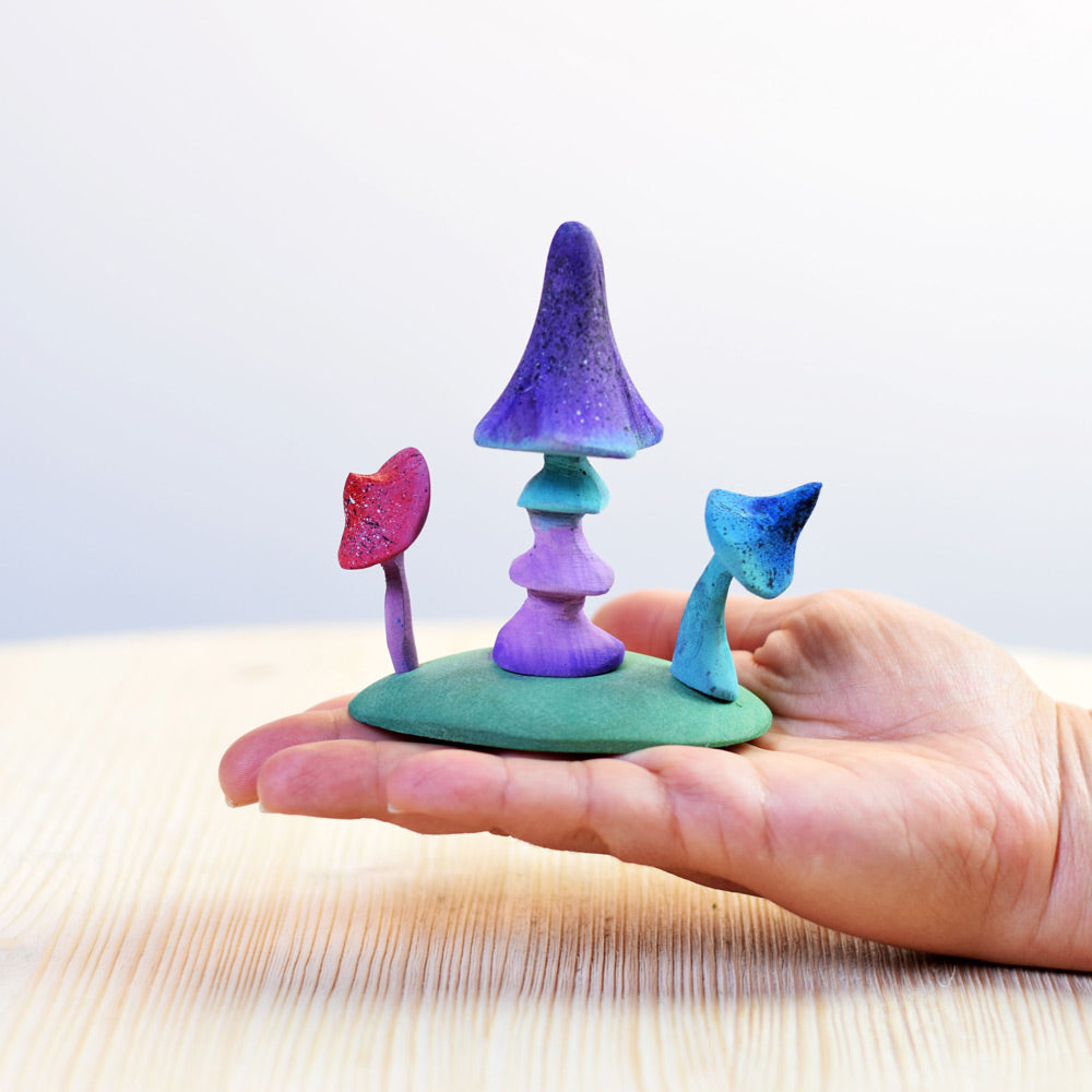 Hand holding the Bumbu rainbow enchanted mushroom toys over a wooden worktop