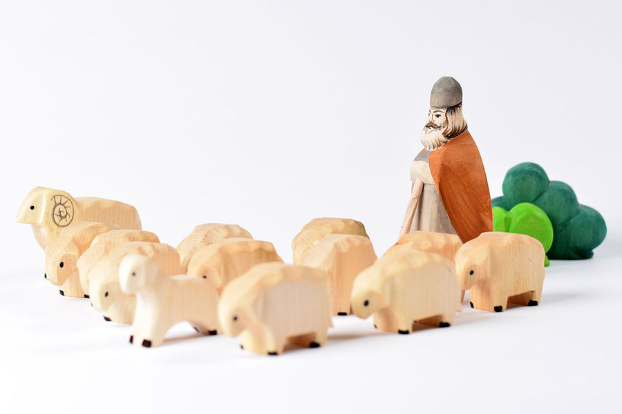 Bumbu eco-friendly wooden shepard with beard figure behind a flock of wooden sheep toys on a white background