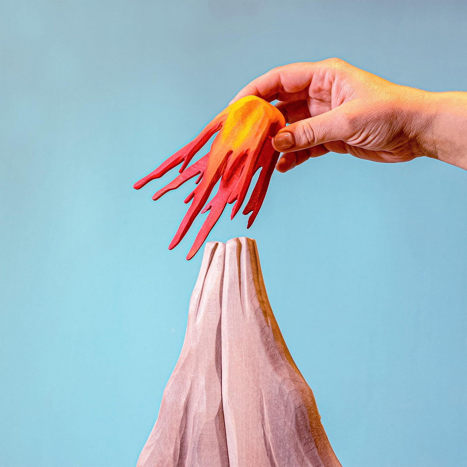 Bumbu Wooden Volcano Set. An adult hand is shown removing the lava section.