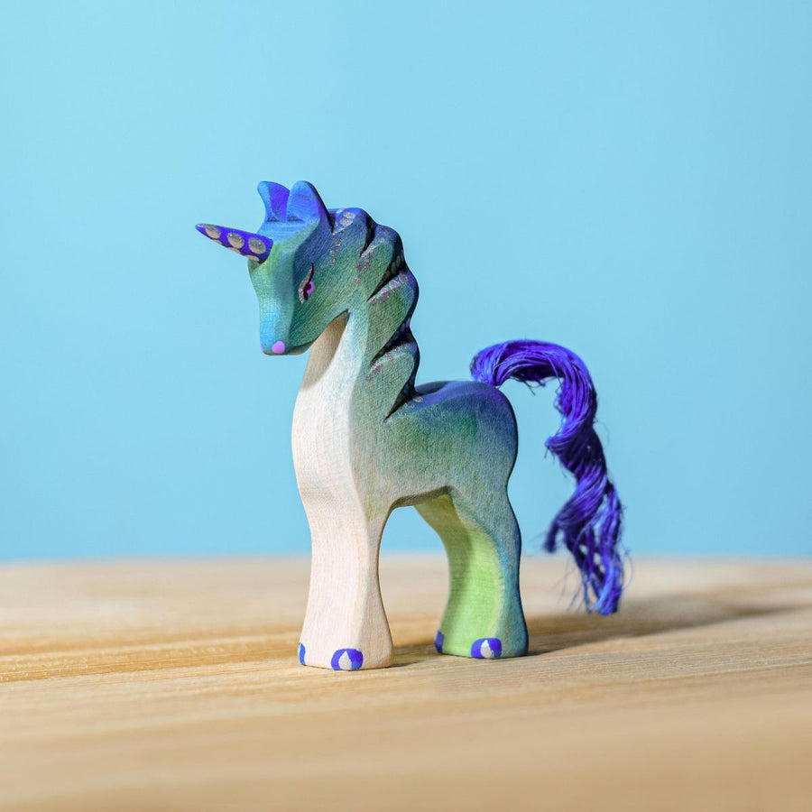 Bumbu green baby unicorn figure pictured on a wooden surface with a blue wall behind