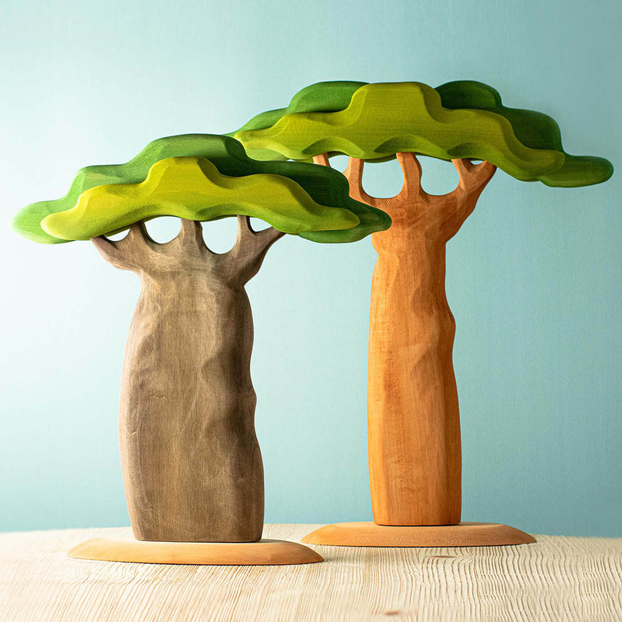 Bumbu hand carved wooden baobab trees with the tall and thick trunks on a wooden table in front of a blue background