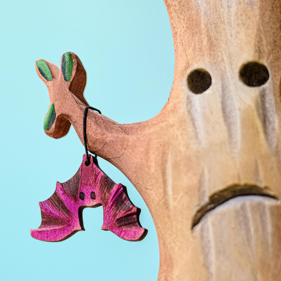 Five Bumbu hand carved Wooden Bat toys hanging upside down from the branches of the Bumbu Large Wooden Spooky Tree. In the background