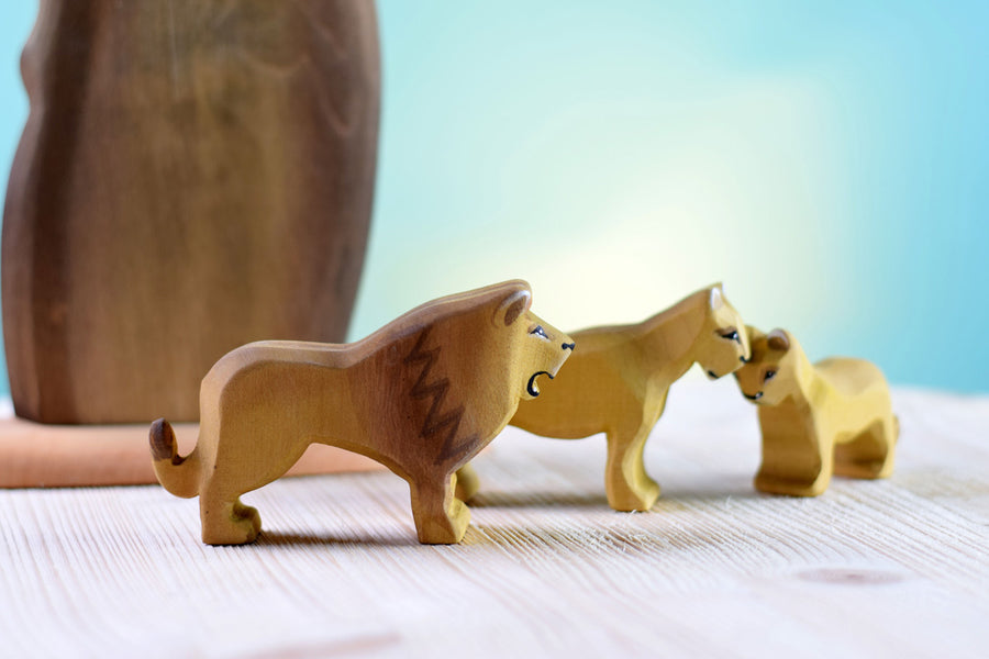 3 Bumbu wooden lion toy figures stood on a wooden worktop in front of a blue background