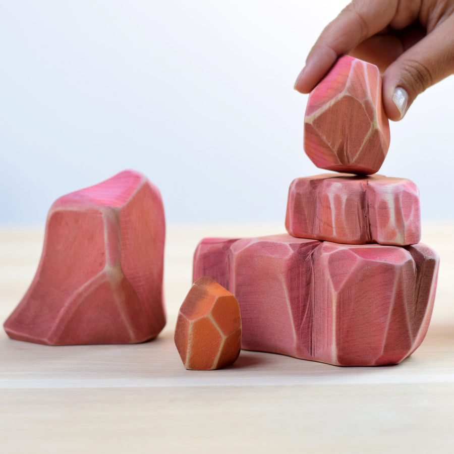 Close up of a hand stacking the Bumbu plastic free Savanna Rocks set on a wooden background