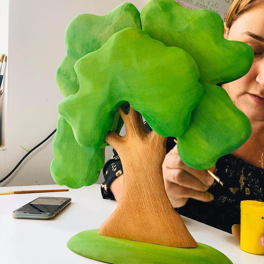 Lady painting the Bumbu large green wooden oak tree with a small brush on a white table