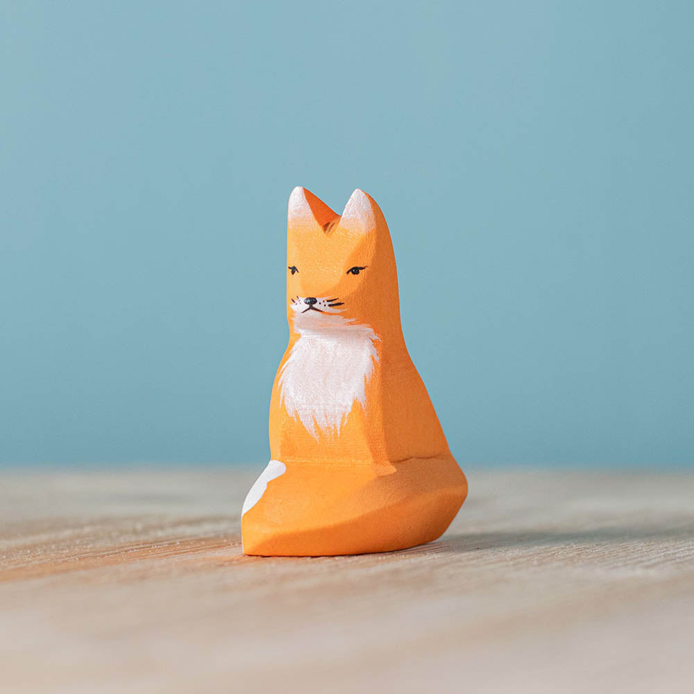 Close up of the Bumbu plastic-free sitting fox toy on a wooden surface in front of a blue background