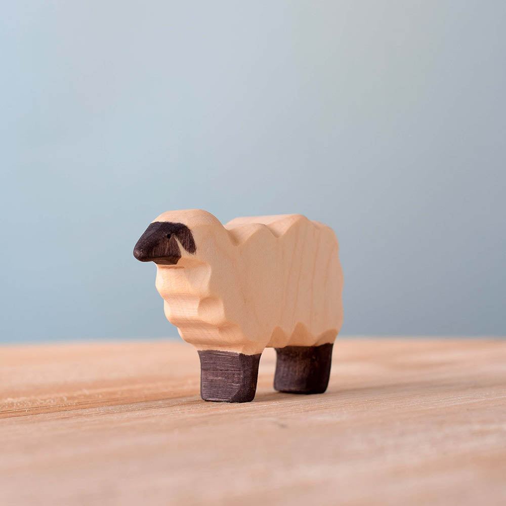 Close up of the plastic-free Bumbu wooden sheep toy figure on a wooden surface in front of a blue background