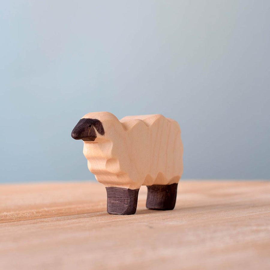 Close up of the plastic-free Bumbu wooden sheep toy figure on a wooden surface in front of a blue background