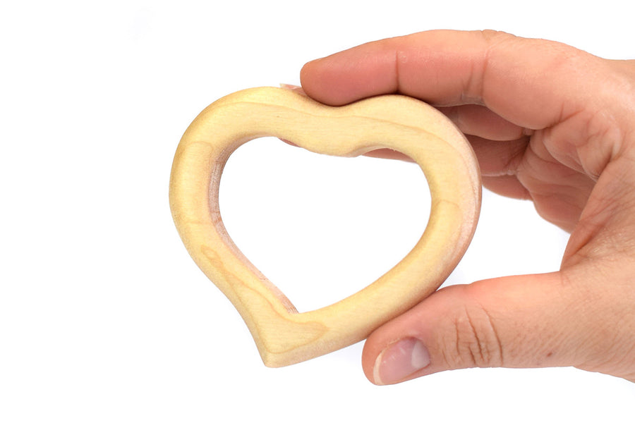 Hand holding the Bumbu handmade wooden baby teething toy heart in front of a white background