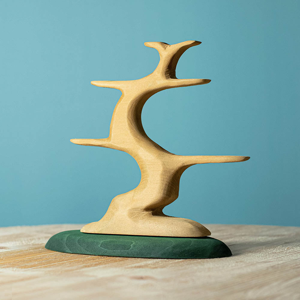 Bumbu handmade wooden bird tree toy figure on a wooden worktop in front of a blue background