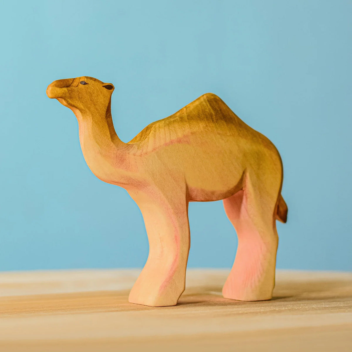 Bumbu handmade wooden camel figure on a blue background and wooden table