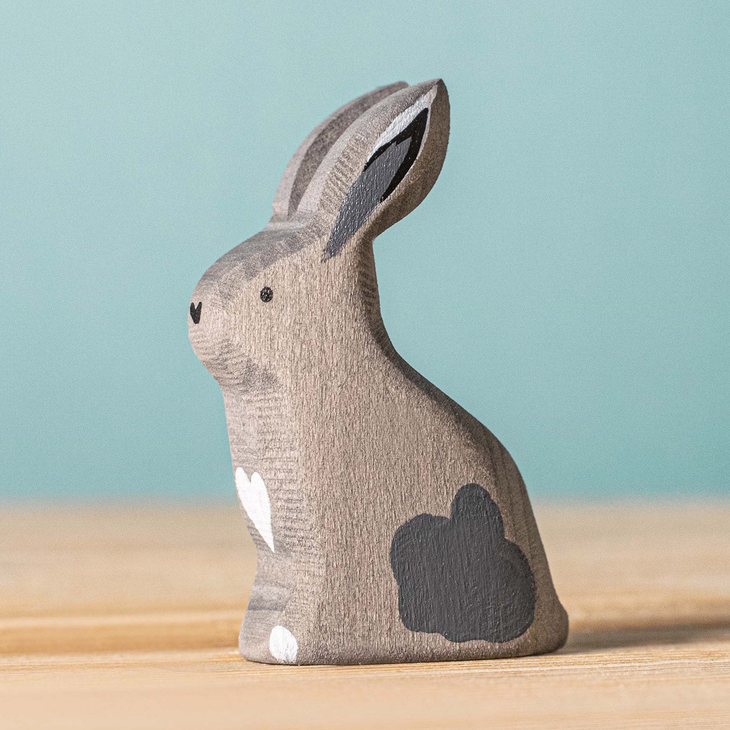 Bumbu Wooden Grey Sitting Rabbit. The toy sits on a wooden surface against a blue background.