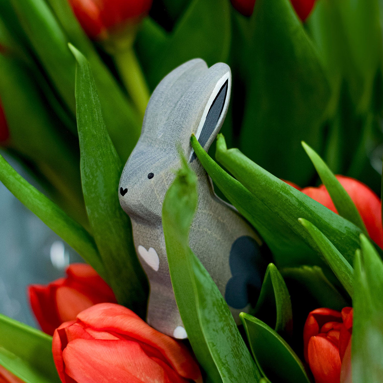 Bumbu Wooden Grey Sitting Rabbit. The toy sits amongst tulips.