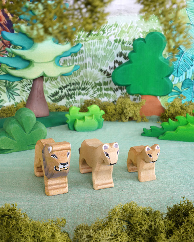 3 wooden Bumbu lion animal figures stood on a wooden worktop in front of a blue background