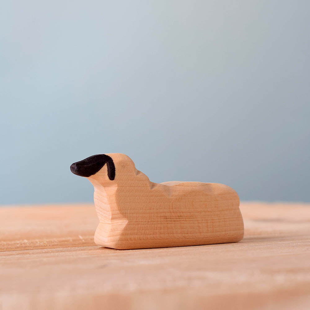 Close up of the Bumbu handmade wooden resting sheep animal figure laying on a wooden surface in front of a blue background