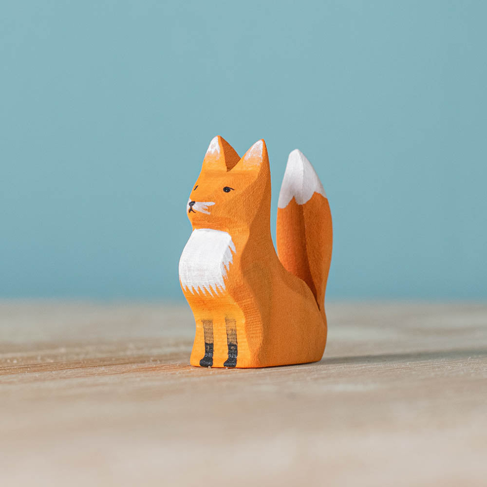 Close up of the Bumbu childrens wooden sitting fox cub figure on a wooden worktop in front of a blue background