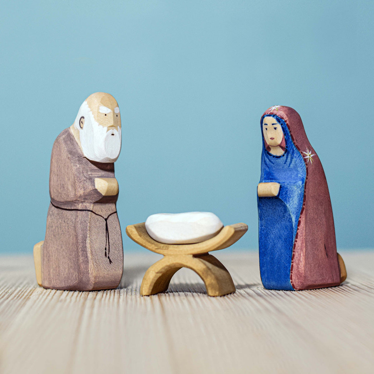 Bumbu Handmade Wooden Mary Figure kneeling down and looking down on the Bumbu Jesus and crib. Mary is kneeling next to the Wooden Joseph figure.