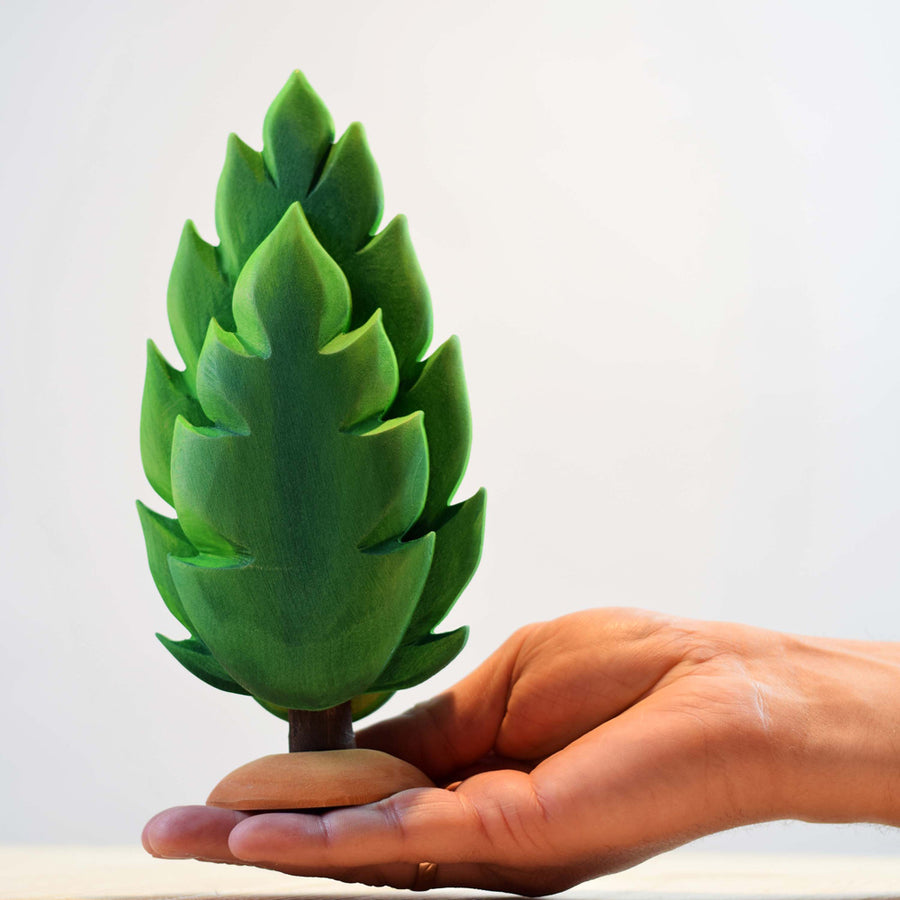 Close up of a hand holding a Bumbu eco-friendly large green wooden thuja tree toy in front of a grey background