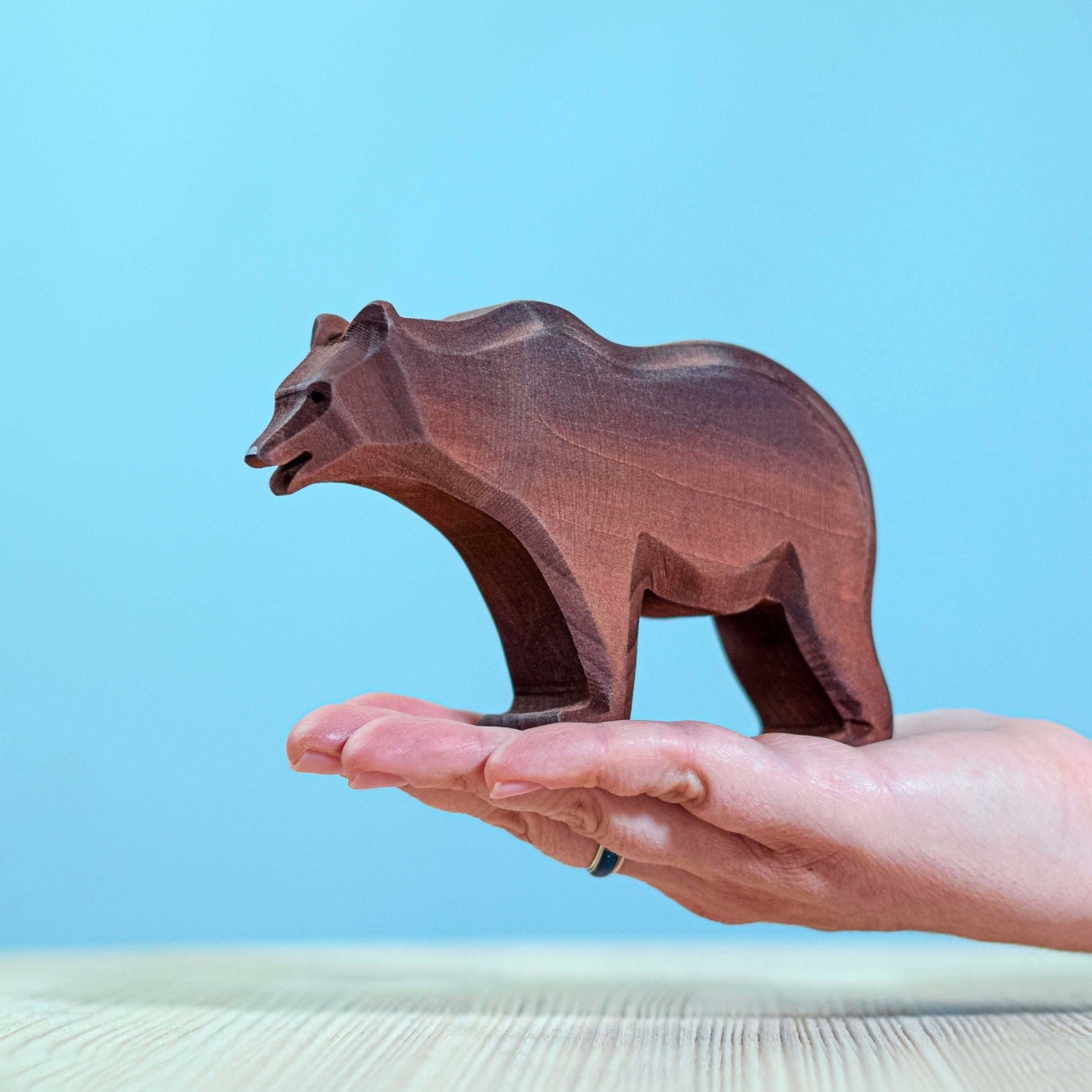 Bumbu large standing wooden bear figure in a persons hand on a blue background