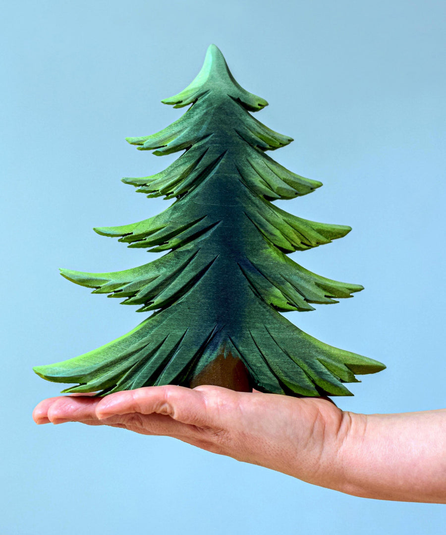 A large Bumbu wooden Fir tree balanced on an adult's hand against a blue background.