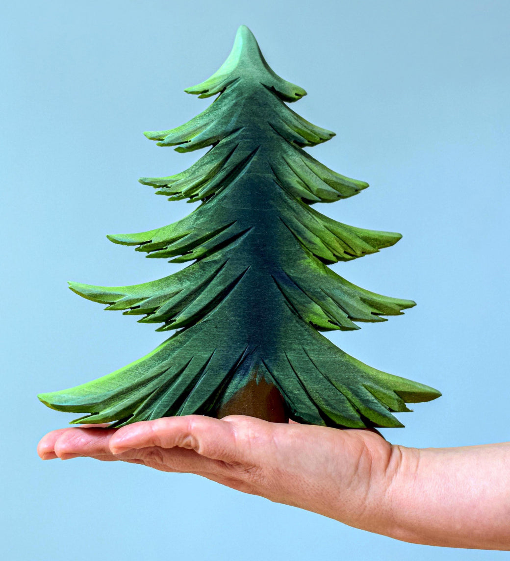 A large Bumbu wooden Fir tree balanced on an adult's hand against a blue background.