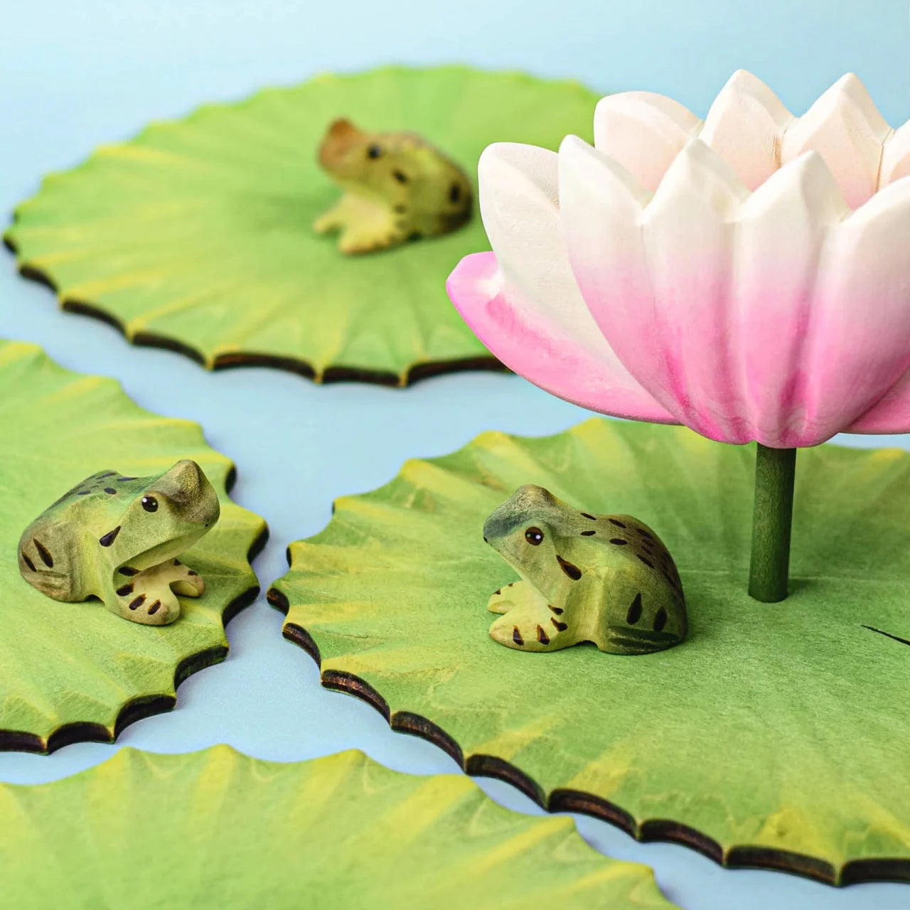 A collecion of 3 Bumbu Frogs on wooden lily pads with a lotus flower.