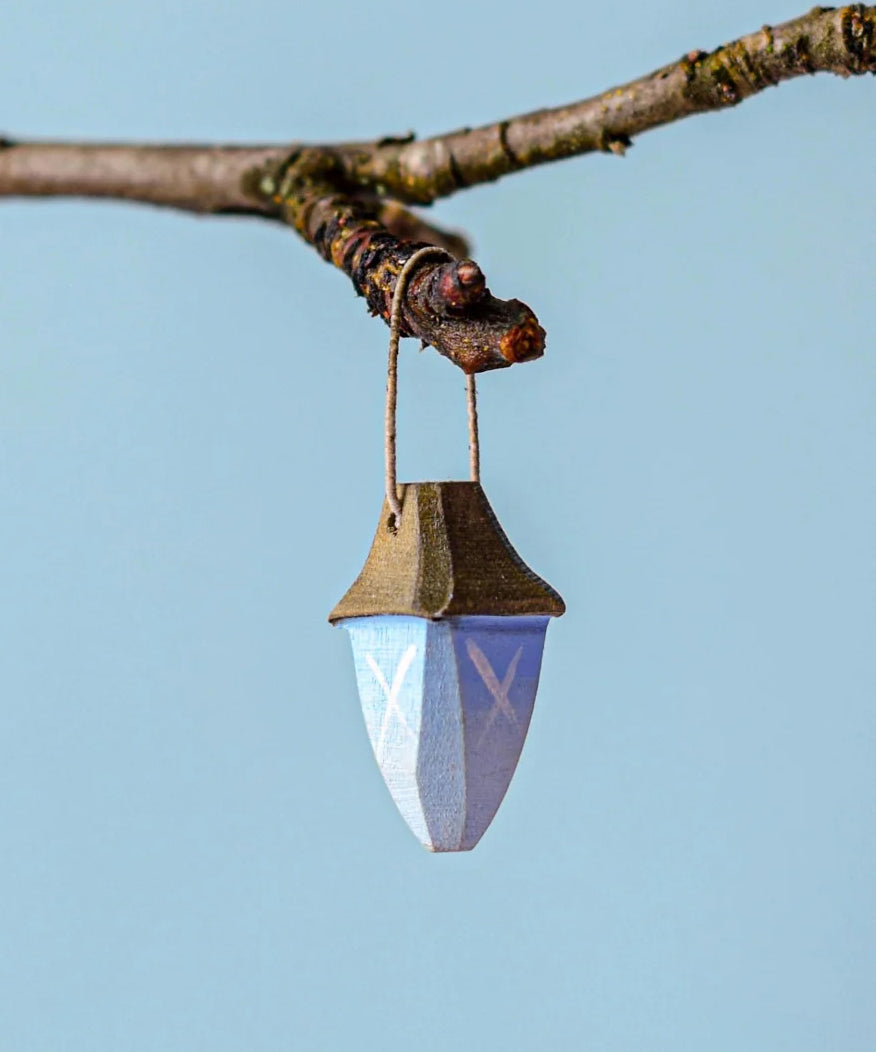 A Bumbu wooden lantern on a twig pictured against a blue background