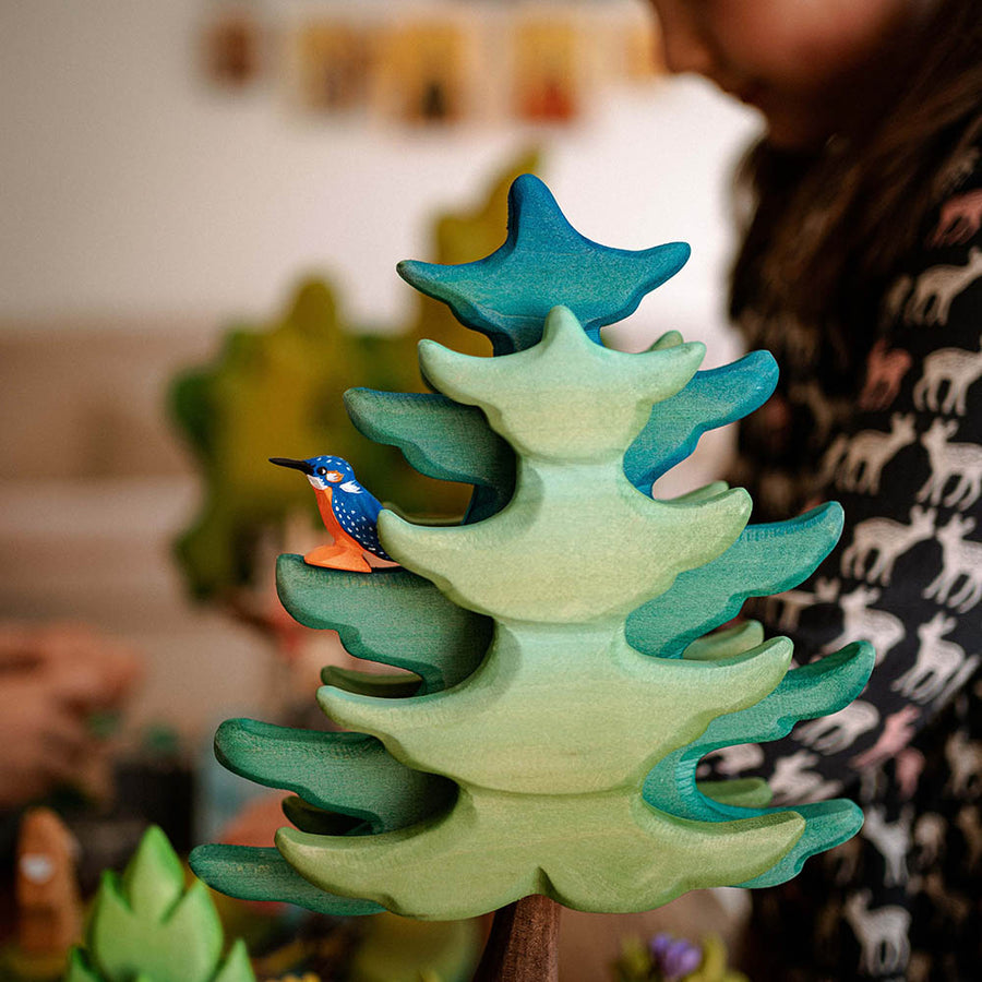 Close up of a Bumbu wooden kingfisher toy figure in the leaves of a green wooden tree toy