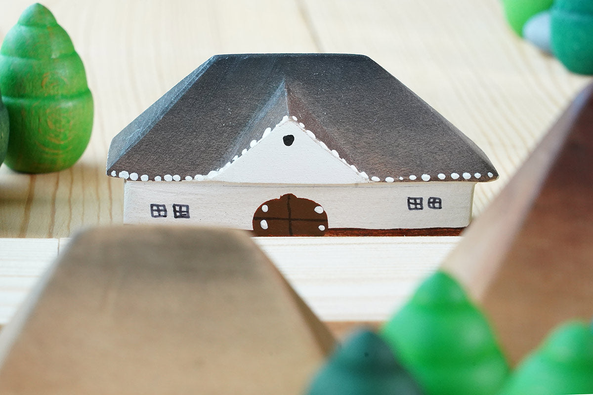 Close up of the Bumbu Muntenia handmade wooden house toy next to some grapat mandala trees