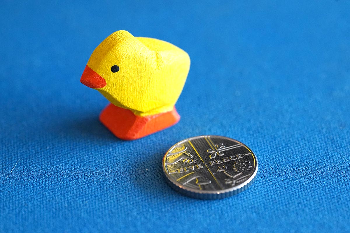 Bumbu eco-friendly wooden chick figure on a blue background next to a 5 pence coin