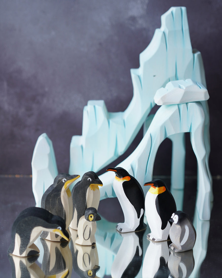 Ostheimer and Holztigher wooden penguin figures placed on a reflective surface with the Bumbu icy cliffs in the background