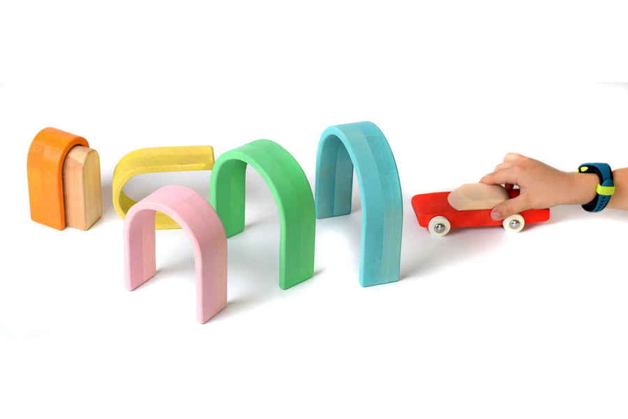 Pieces of the Bumbu wooden pastel arches lined up in a tunnel shape for a little red car toy