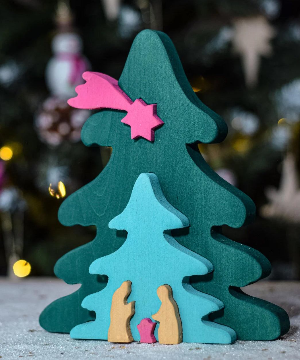 A Bumbu Christmas Tree Nativity Puzzle in a Fuchsia colour way in front of a Christmas tree. 