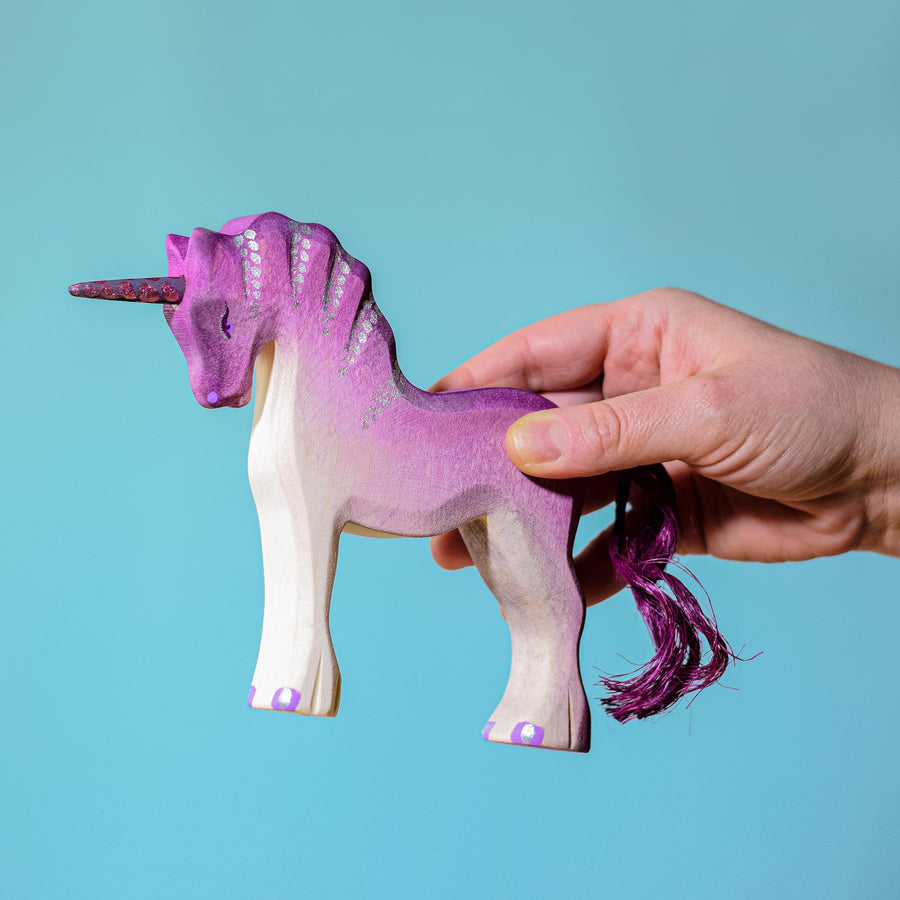 An adult's hand holding the Bumbu Pink Unicorn