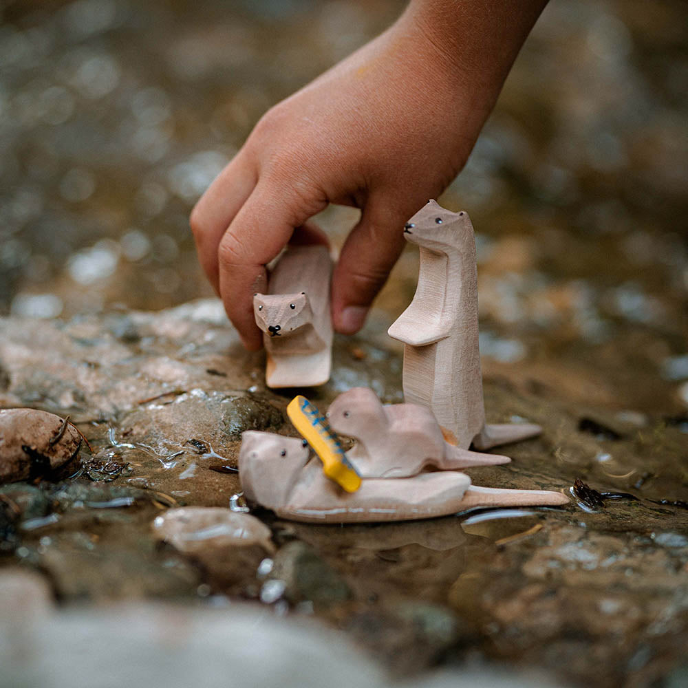 Close up of a childs hand holding the Bumbu handmade otter figure above some rocks in a stream