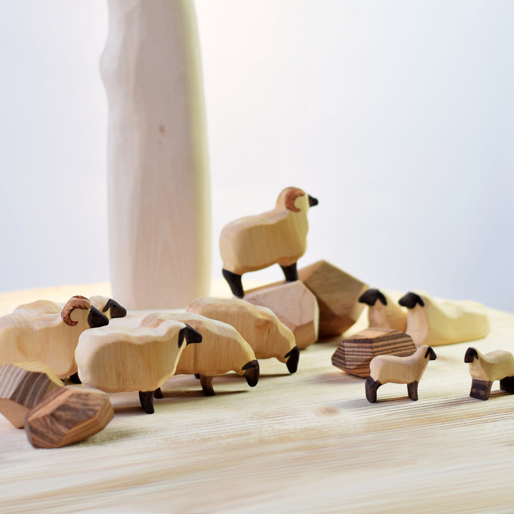 Lots of Bumbu handmade plastic free sheep figures stood on a wooden work top next to a light wooden toy tree