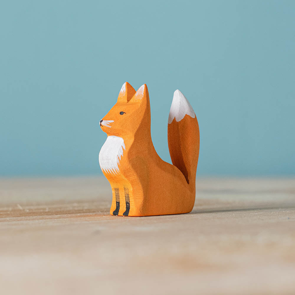 Close up of the Bumbu plastic-free sitting fox cub toy on a wooden worktop in front of a blue background