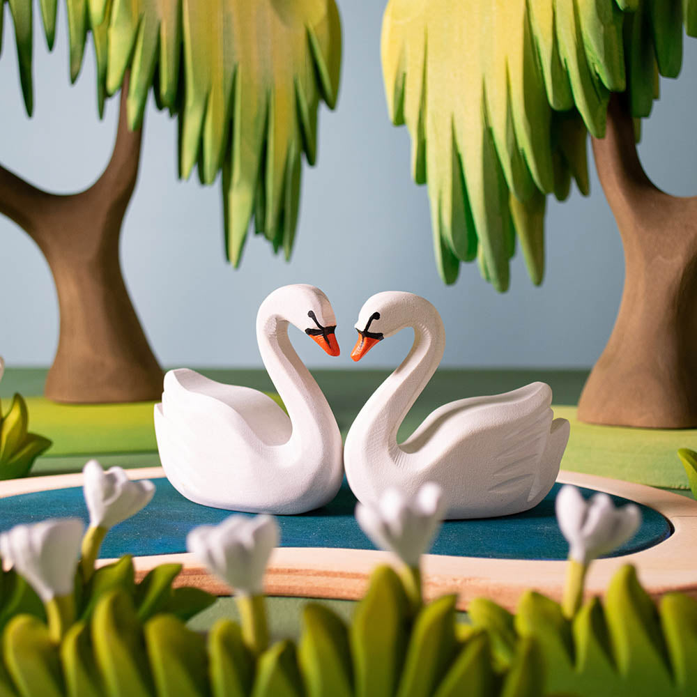 Two Bumbu plastic-free wooden swans face to face on top of the Bumbu heart lake next to some wooden tree toys